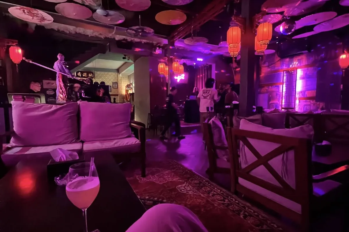 The bar’s low-lit room under hanging paper parasols and red lanterns, with a cocktail on the table in the foreground