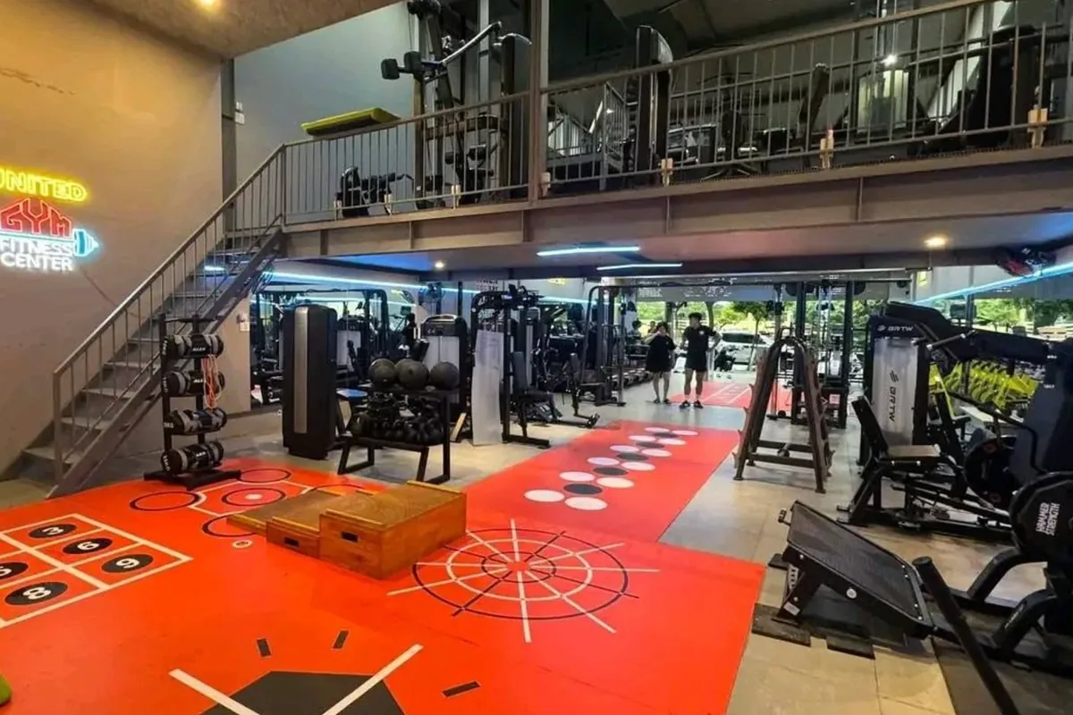 The gym floor with a red functional-training zone, machines along the right and a neon United Gym Fitness Center sign by the stairs