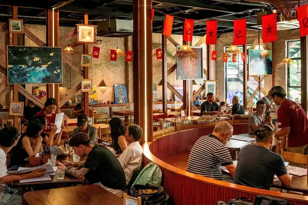 The dining room full of people at wooden tables, with red flags and paintings on the walls