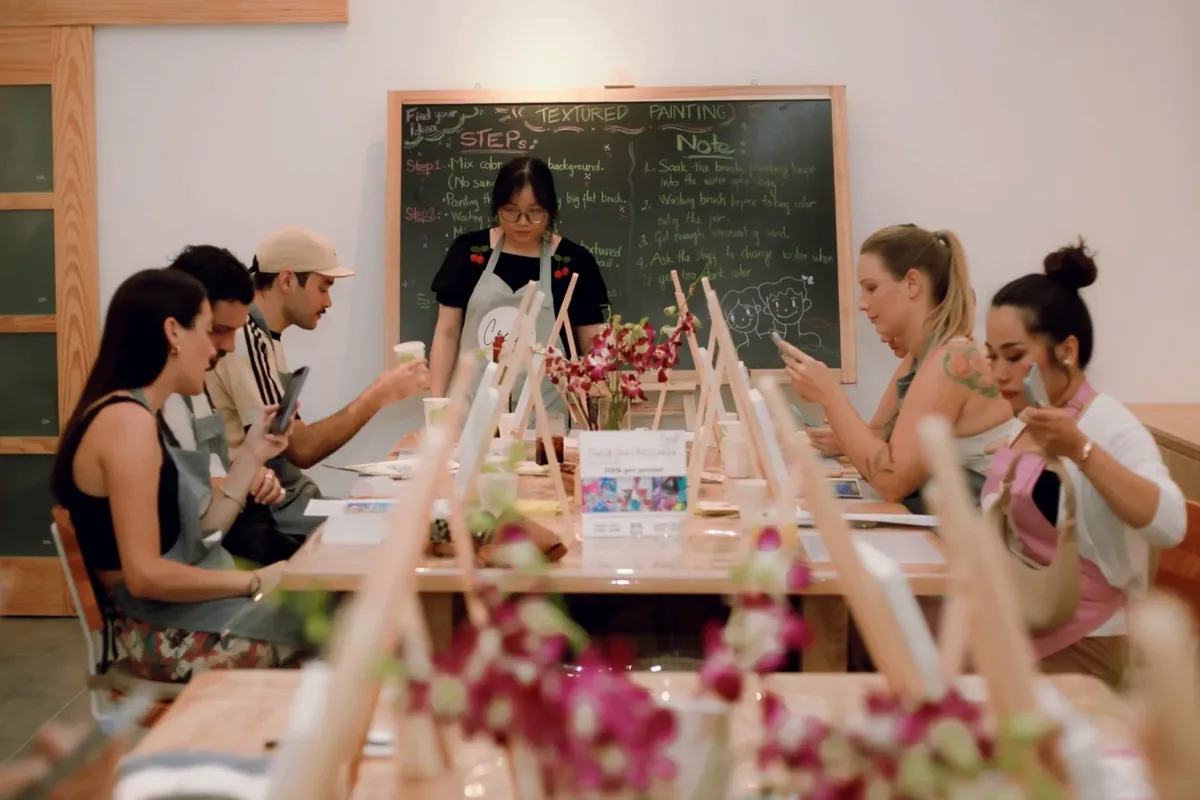 A textured-painting class at a long wooden table, with easels and orchids down the middle and the steps written on a blackboard