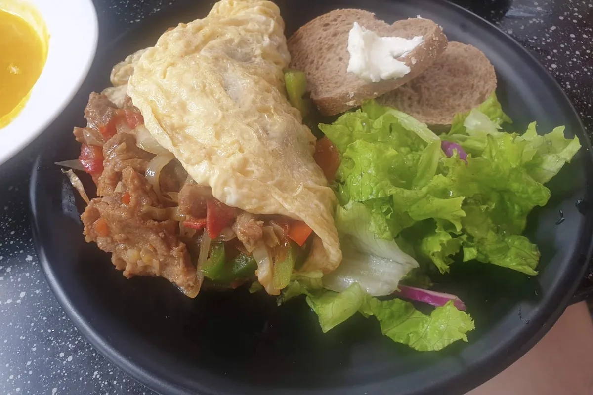 A steak and pepper omelette with salad and toast, photographed at the table