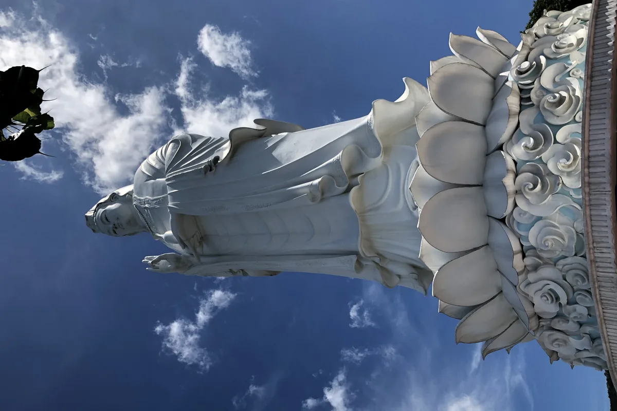 The white Lady Buddha statue seen from below against a blue sky with clouds