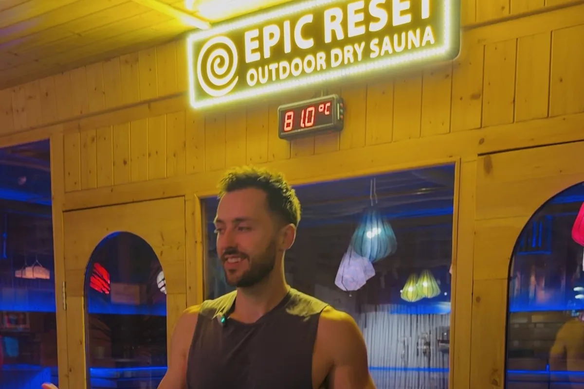 Jake outside the timber sauna cabin under its lit Epic Reset sign, with the thermometer reading 81°C