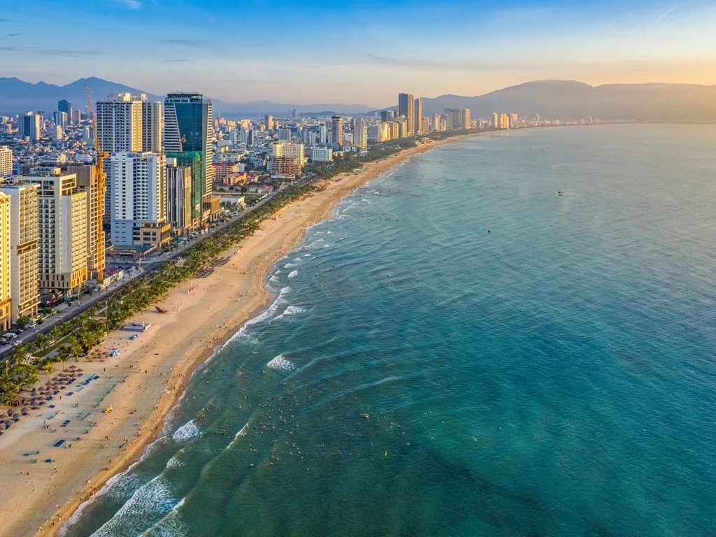 Beachfront buildings beside a long sandy beach and blue sea.