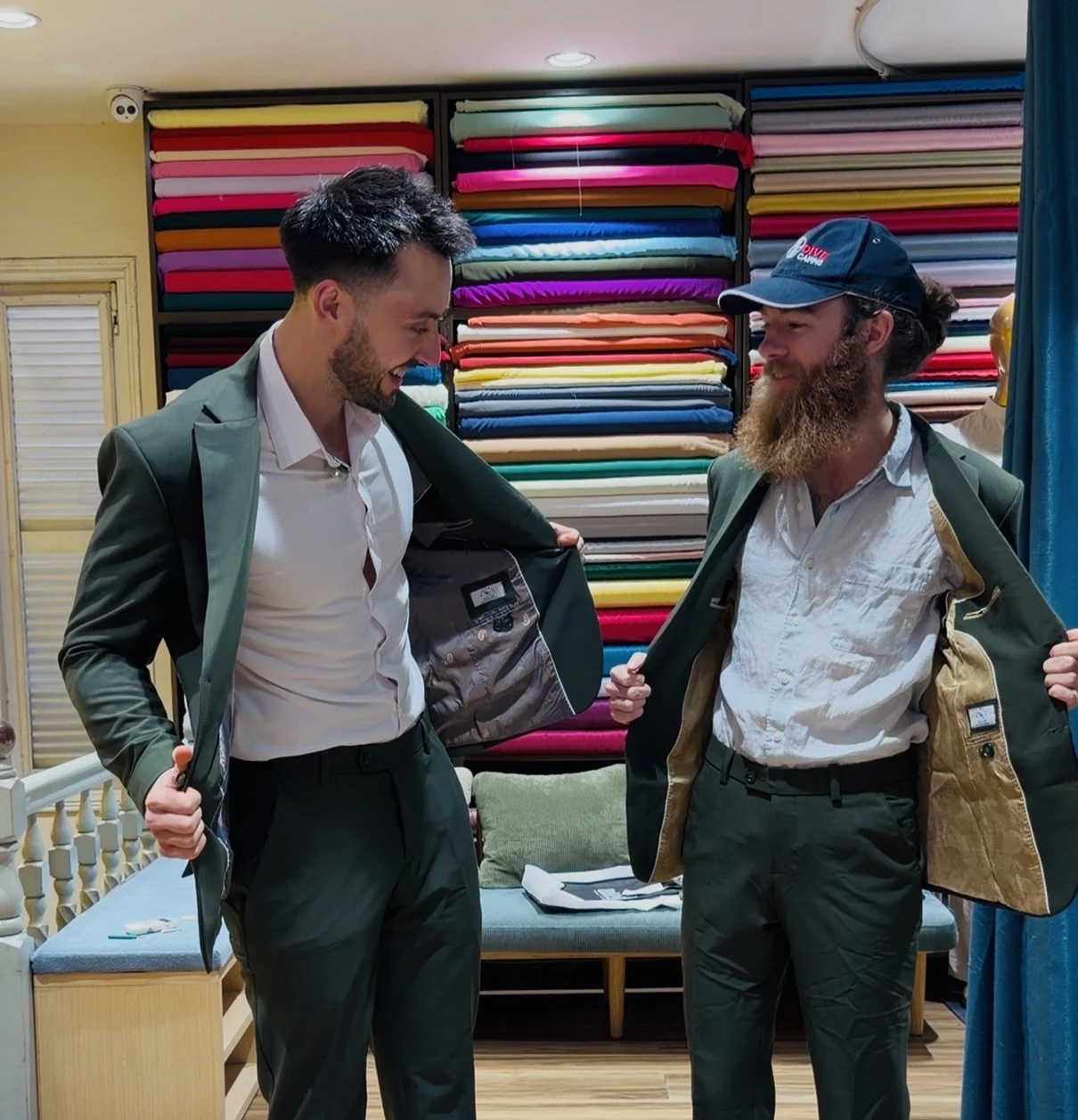 Jake and a friend smiling and showing their suit jackets in a tailor’s shop